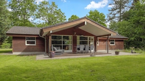 Une maison à deux étages avec un patio couvert, de grandes fenêtres et une pelouse.