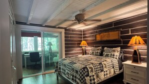 Un dormitorio con cama, dos lámparas de noche, un ventilador de techo y vistas al balcón a través de un ventanal.