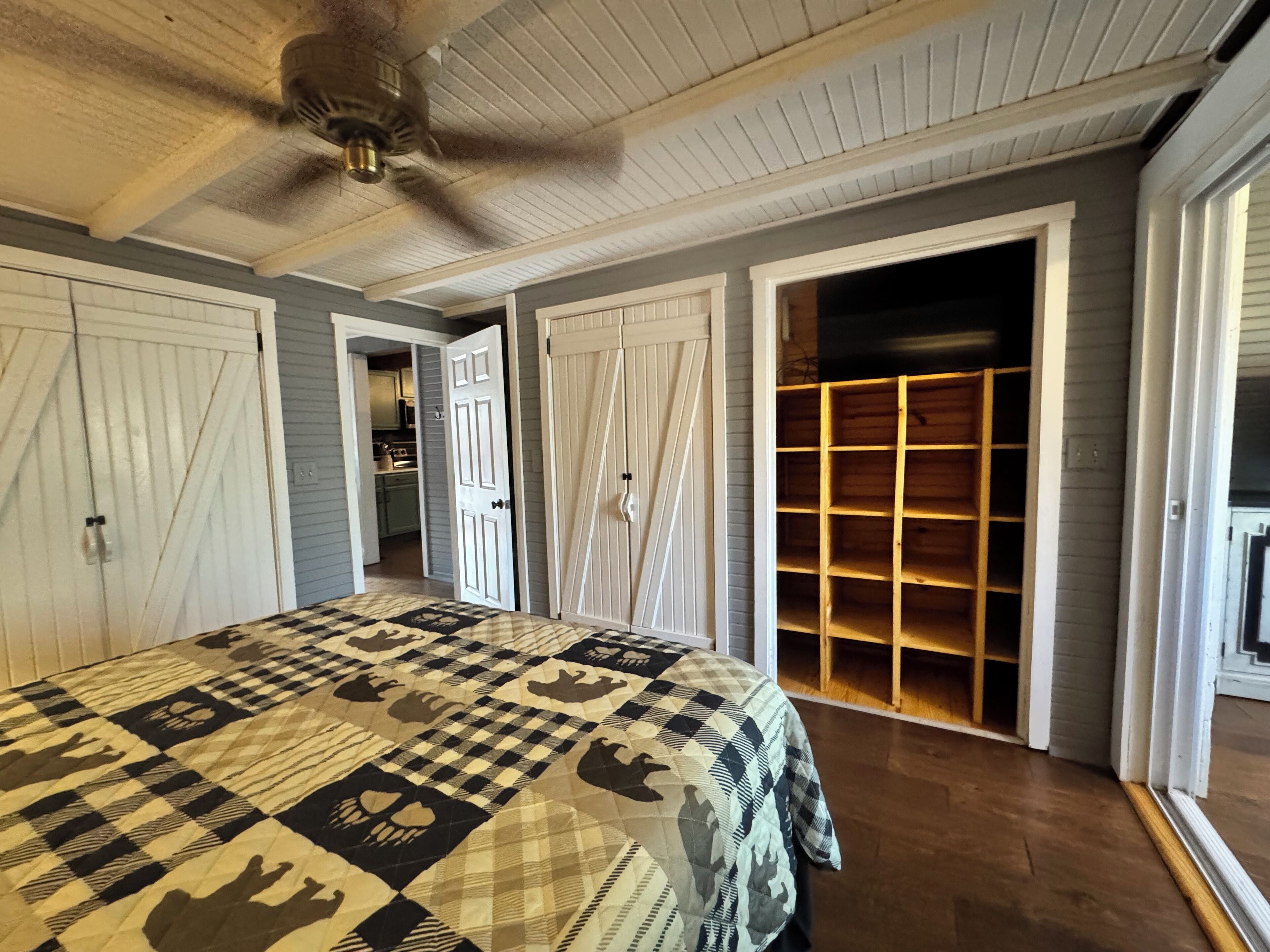 Une chambre avec un grand lit, un ventilateur de plafond et un dressing avec des étagères en bois.