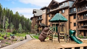 Eine Lodge mit Spielbereich, der eine Bärenskulptur, eine Rutsche und eine Kletterkonstruktion zeigt.