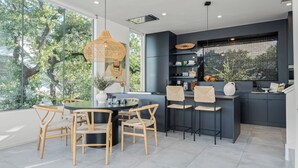 A modern kitchen with a dining area, large windows, and a view of trees. - Pool, Putting Green, Game Room, Rooftop Bouldin Collective 902a by Avantstay (Austin)