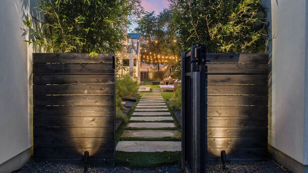 A wooden gate leading to a pathway with a garden and a building in the background. - Pool, Putting Green, Game Room, Rooftop Bouldin Collective 902a by Avantstay (Austin)