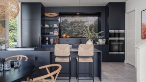 A modern kitchen with dark cabinetry, a central island with bar stools, a large window with a view, and built-in appliances. - Pool, Putting Green, Game Room, Rooftop Bouldin Collective 902a by Avantstay (Austin)