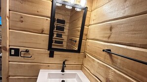 A wooden-paneled bathroom with a white sink, a mirror, and a towel rack. - Cabin 1 on The Willow Reservoir (Hazelhurst)