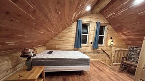 A cozy attic bedroom with a wooden sloped ceiling, a single bed, a small wooden table, and a window with curtains. - Cabin 1 on The Willow Reservoir (Hazelhurst)