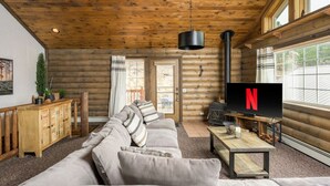 Ein rustikaler Innenraum einer Blockhütte mit Sofa, Fernseher und Kamin.