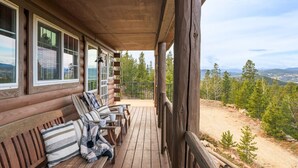 Eine Blockhütte mit einer Holzterrasse, Sitzgelegenheiten im Freien und einem schönen Bergblick.