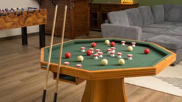 Una mesa de billar con bolas, una mesa de futbolín y un sofá en una habitación con suelo de madera.