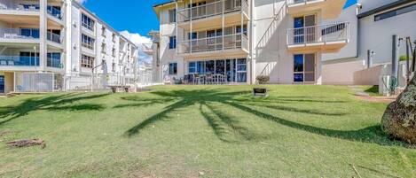 A multi-story residential building with balconies, a grassy courtyard, and a clear blue sky.
