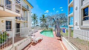 A pool area with a clear view of the ocean, surrounded by buildings with balconies and a fenced patio area. - Shoreline Apartments - Unit 9 (Bargara)