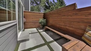 Une terrasse avec un banc en bois, une petite table et un pot de fleurs.