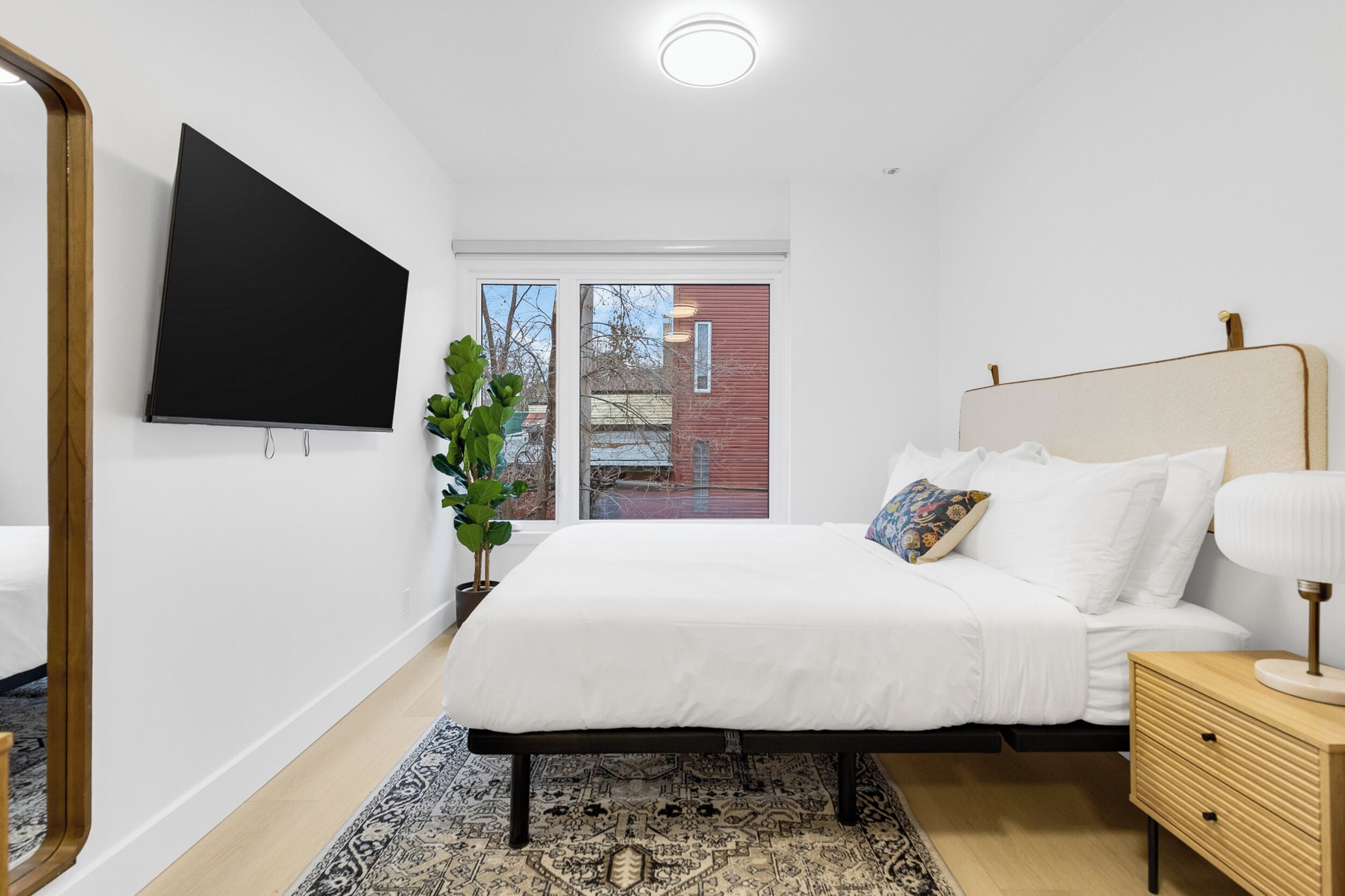Quarto moderno com cama, mesa de cabeceira e televisão na parede.