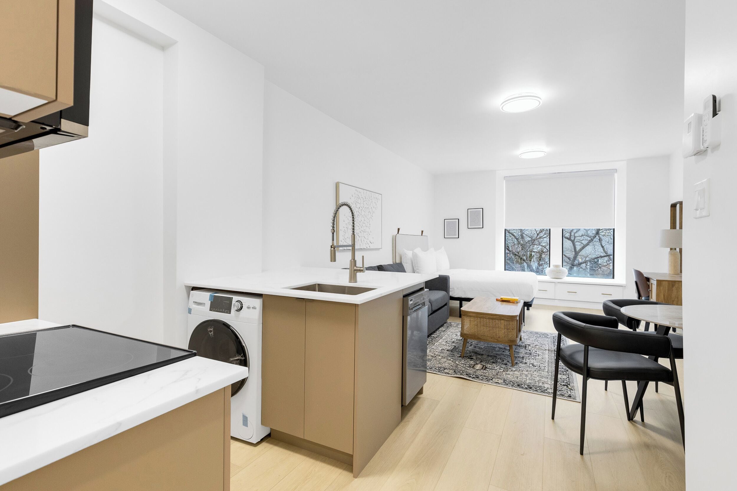 Cocina compacta con lavadora, zona de comedor con mesa y sillas, y cama al fondo.