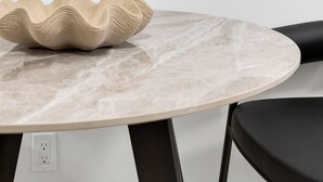 Un tavolo rotondo in marmo con una ciotola beige, una sedia nera e un quadro astratto incorniciato al muro.