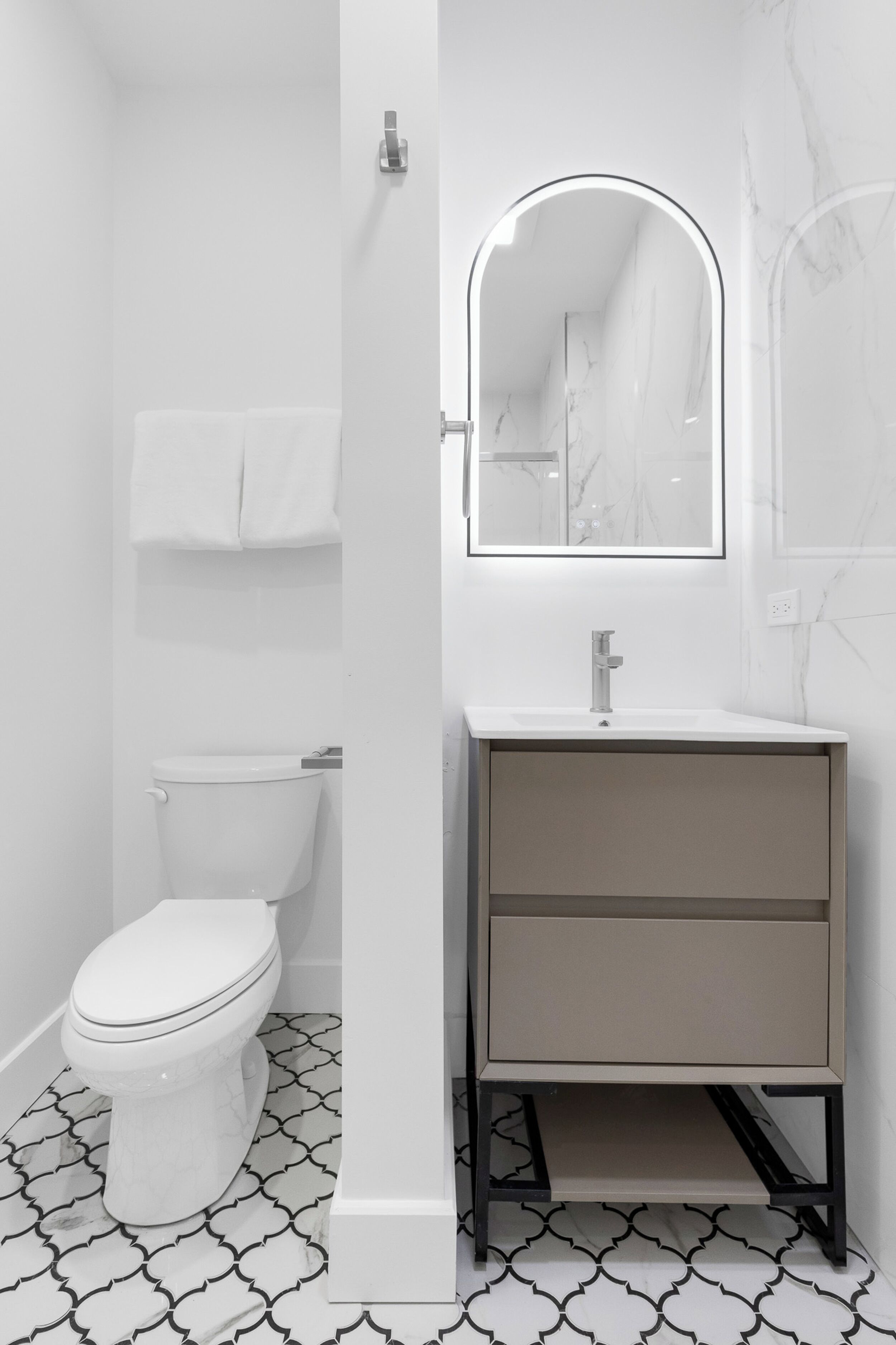 A modern bathroom with a toilet, a sink with a mirror, and patterned floor tiles.