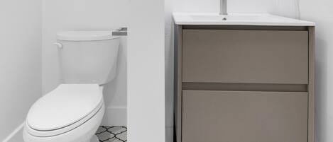 A modern bathroom with a toilet, a sink with a mirror, and patterned floor tiles.