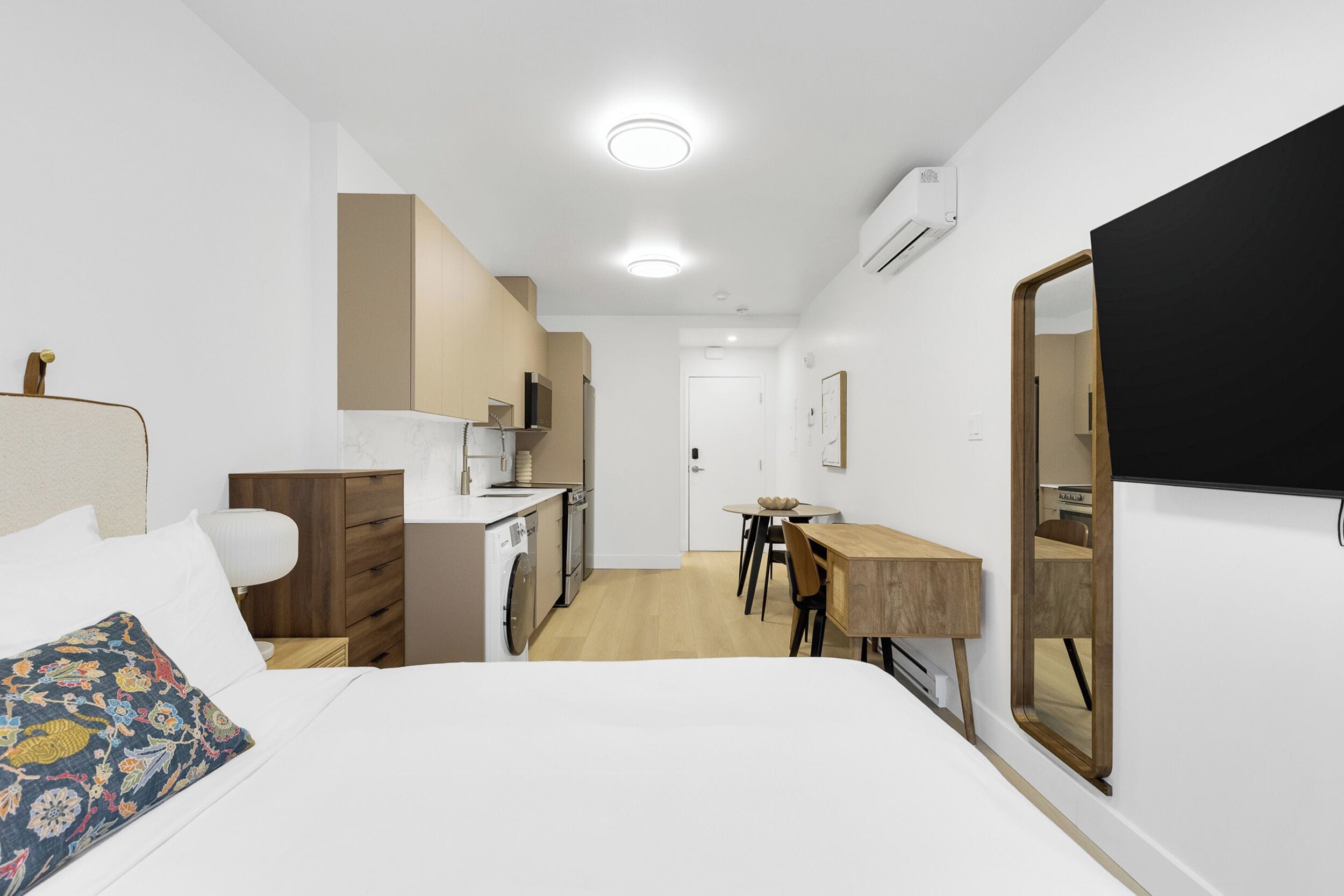 Une chambre d’hôtel moderne comprenant un lit, une commode en bois, un petit coin cuisine et une table à manger.