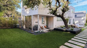 A modern house with a well-maintained lawn, outdoor seating area, and a tree in the front yard.