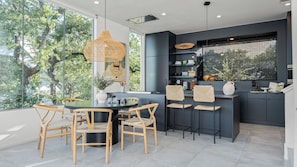 A modern kitchen with a dining area, large windows, and a view of trees.