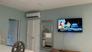 Een hotelkamer met een bed, een houten stoel, een televisie aan de muur en een airconditioning.