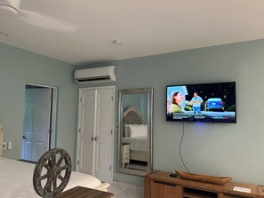 Ein Hotelzimmer mit einem Bett, einem Holzstuhl, einem Fernseher an der Wand und einer Klimaanlage.