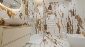 A modern bathroom with a marble backsplash, a freestanding bathtub, and a vanity with a bowl sink.