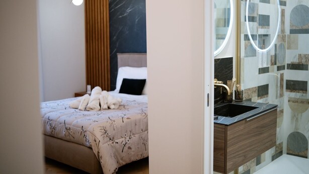 A hotel room with a bed, a bedside table, and a bathroom with a sink and mirror.