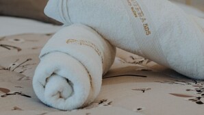 Two rolled white towels on a bed with a floral pattern bedspread.
