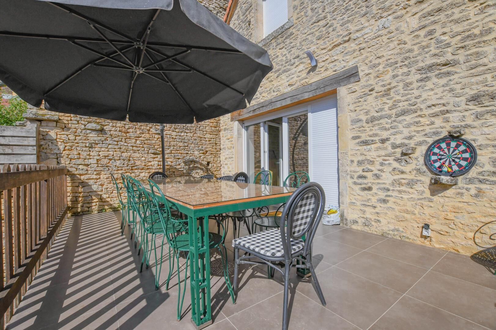 A stone building with a table and chairs, a dartboard, and a large umbrella.