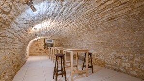 A stone-walled room with a long wooden table and stools, a tiled floor, and a ceiling light fixture. - Le Grand Gite du Relais (PARGUES)