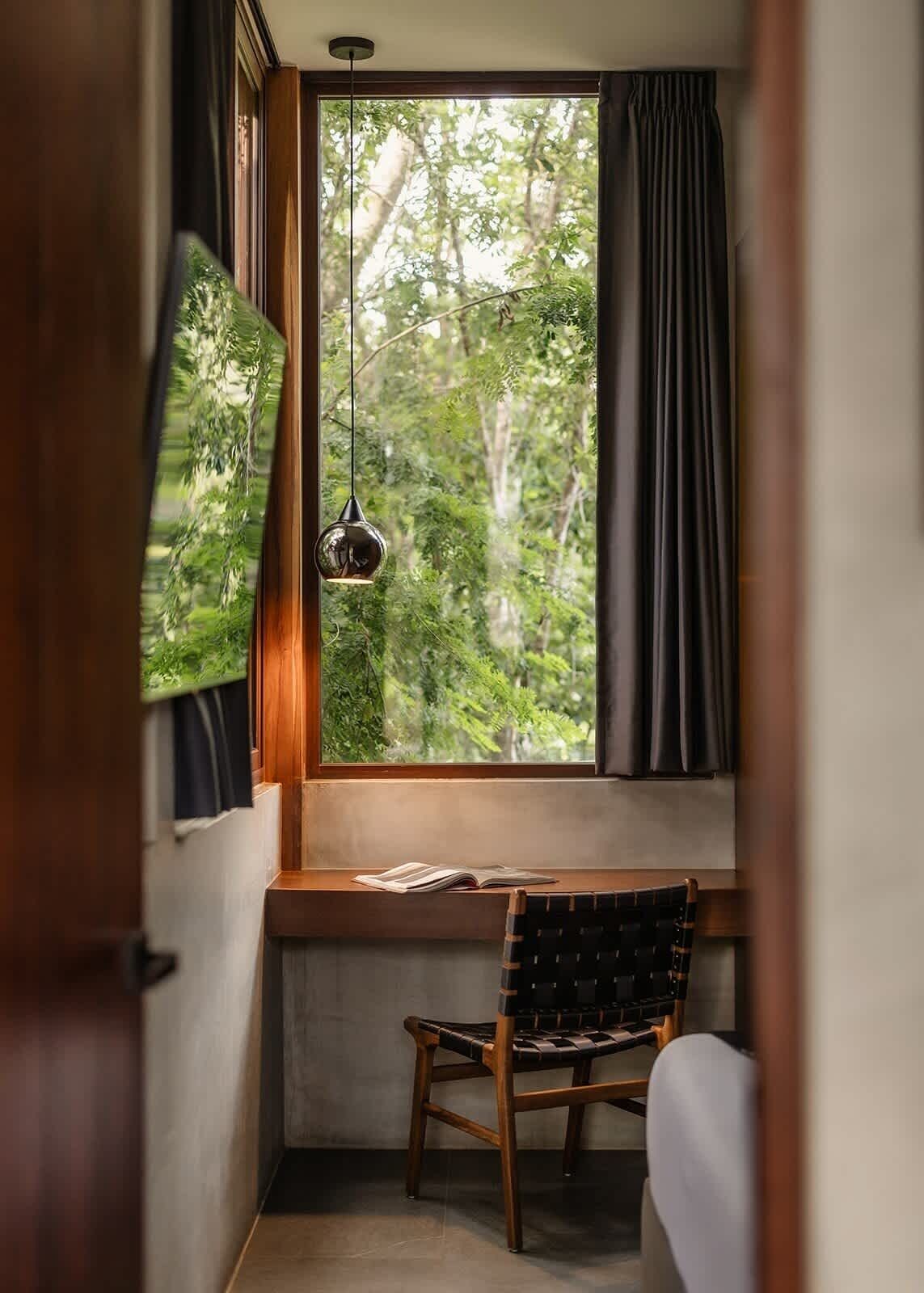 A room with a window, a hanging light fixture, a chair, and a table.