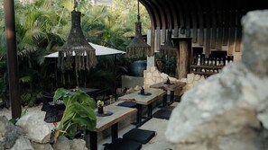 An outdoor dining area with tables, chairs, hanging lamps, and a bar area with bottles. - Siwa Jungle Escape B1-101 Beach Club Access (Tulum)