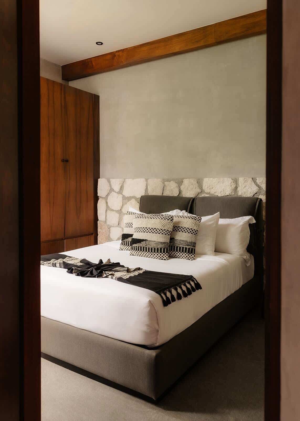 Quarto com cama, parede de pedra e mobiliário de madeira.