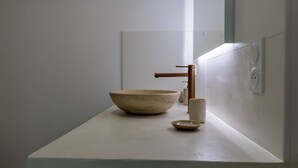 Une salle de bain minimaliste avec un grand lavabo en céramique, un robinet en cuivre et un petit bol posé sur un plan de travail blanc.