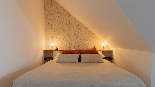Une chambre à coucher avec un grand lit, deux tables de chevet et un mur orné d’un motif floral.