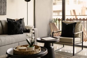 A modern living room with a sofa, a chair, a small round table, and a window with a view of the outside. - The Chloe Ocean Views Jacuzzi Close to Beach! (Tulum)