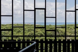 A view through a window with a grid pattern, revealing a landscape with dense greenery and a distant body of water. - The Chloe Ocean Views Jacuzzi Close to Beach! (Tulum)