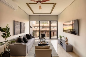 A modern living room with a sofa, armchair, coffee table, and a TV mounted on the wall. - The Chloe Ocean Views Jacuzzi Close to Beach! (Tulum)
