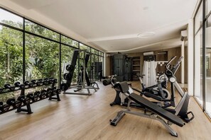A gym with weightlifting equipment, cardio machines, and large windows offering a view of greenery. - The Chloe Ocean Views Jacuzzi Close to Beach! (Tulum)