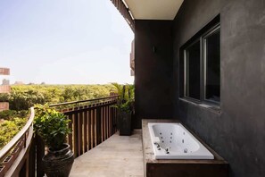 A balcony with a bathtub, potted plants, and a view of greenery. - The Chloe Ocean Views Jacuzzi Close to Beach! (Tulum)