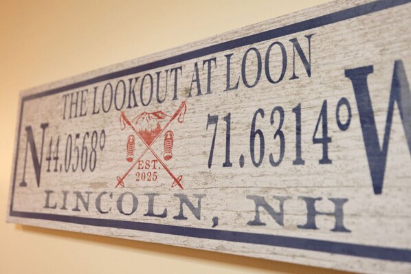 A wooden sign with the text "The Lookout at Loon, Lincoln, NH" and a compass rose with a red "N" and "W" indicating north and west directions. - Slope Views- Ski Shuttle- Pool & Hot Tub (Lincoln)