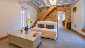 A cozy living room with a sofa, coffee table, and a staircase leading to an upper level. - Le Petit Gite du Relais (PARGUES)