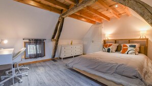 A bedroom with a sloped ceiling, a desk, a dresser, and a bed with decorative pillows. - Le Petit Gite du Relais (PARGUES)