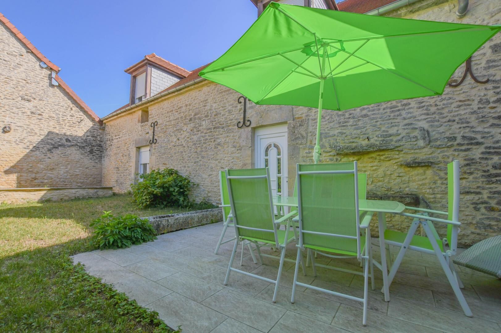 A patio with a table and chairs, a green umbrella, and a stone building in the background.