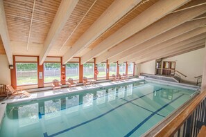 Ein Innenpool mit Holzbalken, klarem Wasser und mehreren Liegestühlen entlang des Randes.