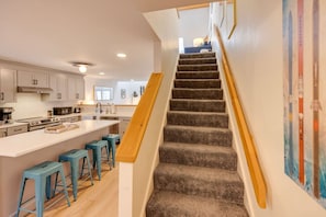 Eine moderne Küche mit einer zentralen Kochinsel, einer Treppe mit Holzhandläufen und Blick ins Wohnzimmer.