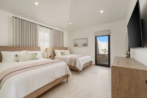 A bedroom with two beds, a wooden dresser, a flat-screen TV, and a large window with curtains. - Ocean View 3 BR Penthouse with Private Jacuzzi at Puerta del Sol, Cabo San Lucas (Cabo San Lucas)