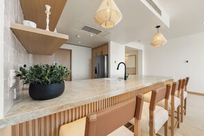 A modern kitchen with a marble countertop, wooden bar stools, and pendant lighting. - Ocean View 3 BR Penthouse with Private Jacuzzi at Puerta del Sol, Cabo San Lucas (Cabo San Lucas)