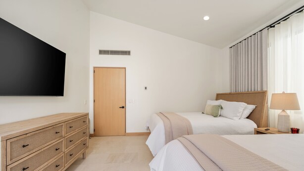 Habitación de hotel con dos camas, un aparador de madera, un televisor de pantalla plana, una lámpara de noche y una ventana con cortinas.