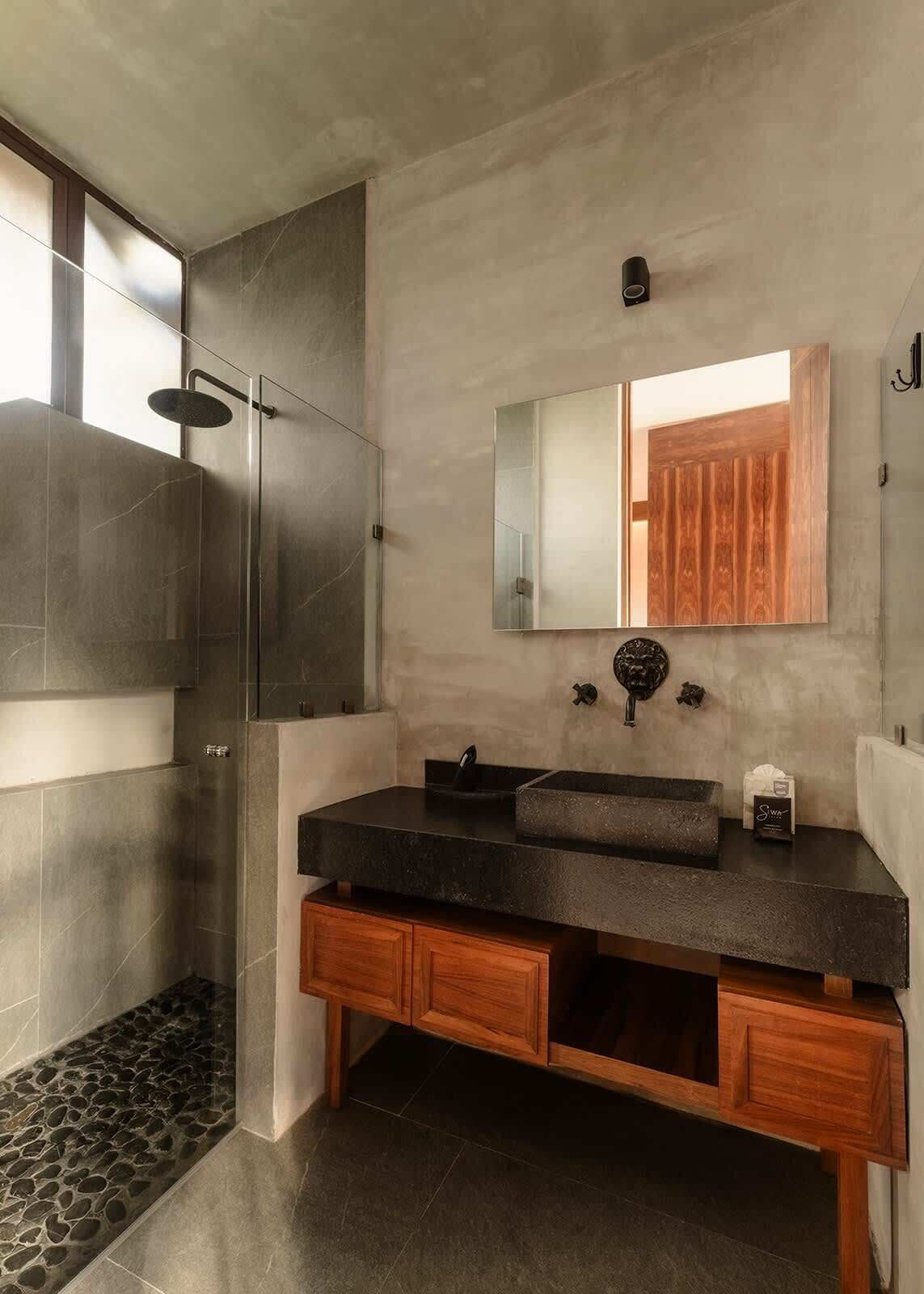 Un baño moderno con un espejo grande, un lavabo negro y una zona de ducha.